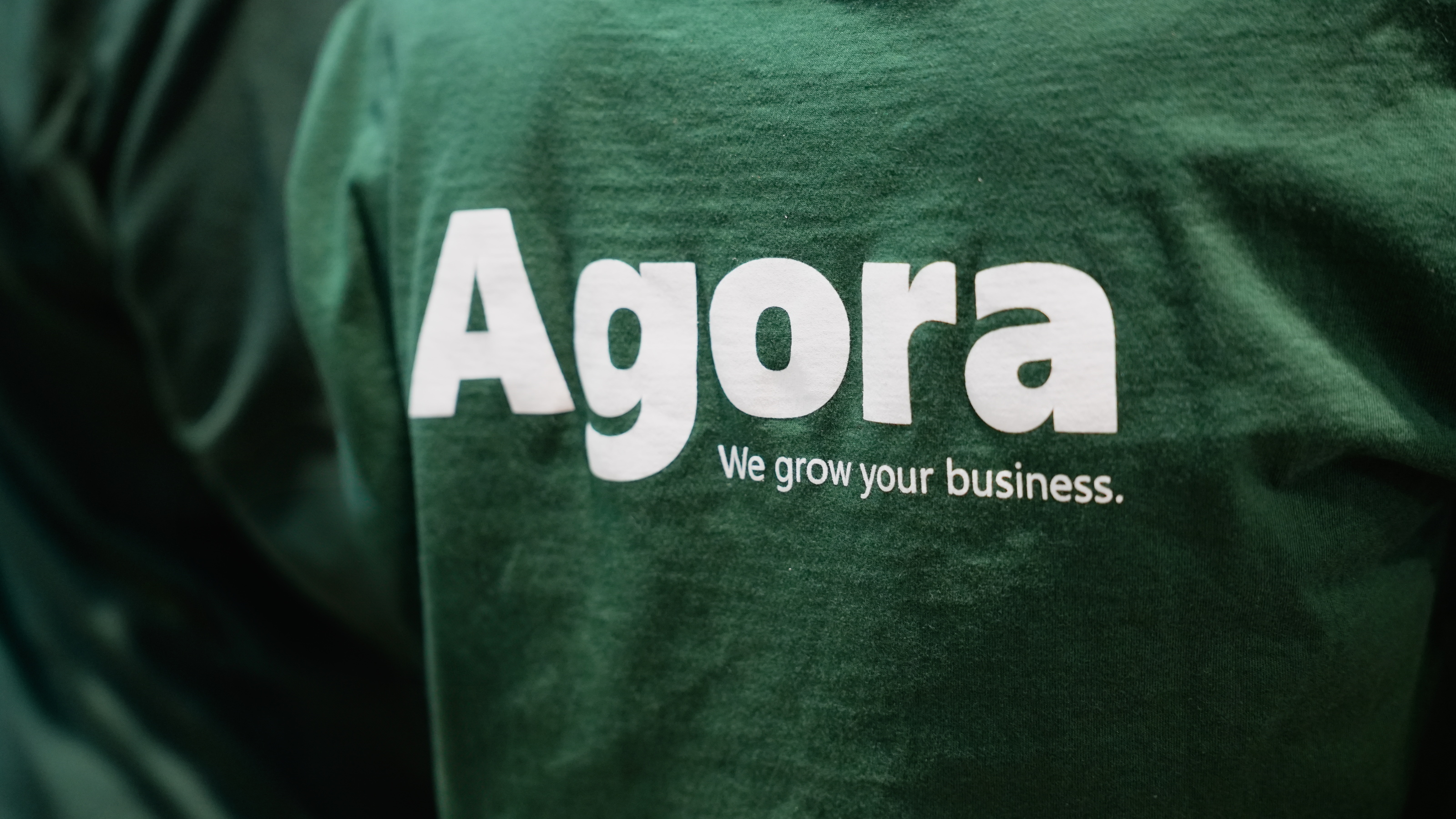 Groene hoodie met wit Agora-logo en slogan op de rug.