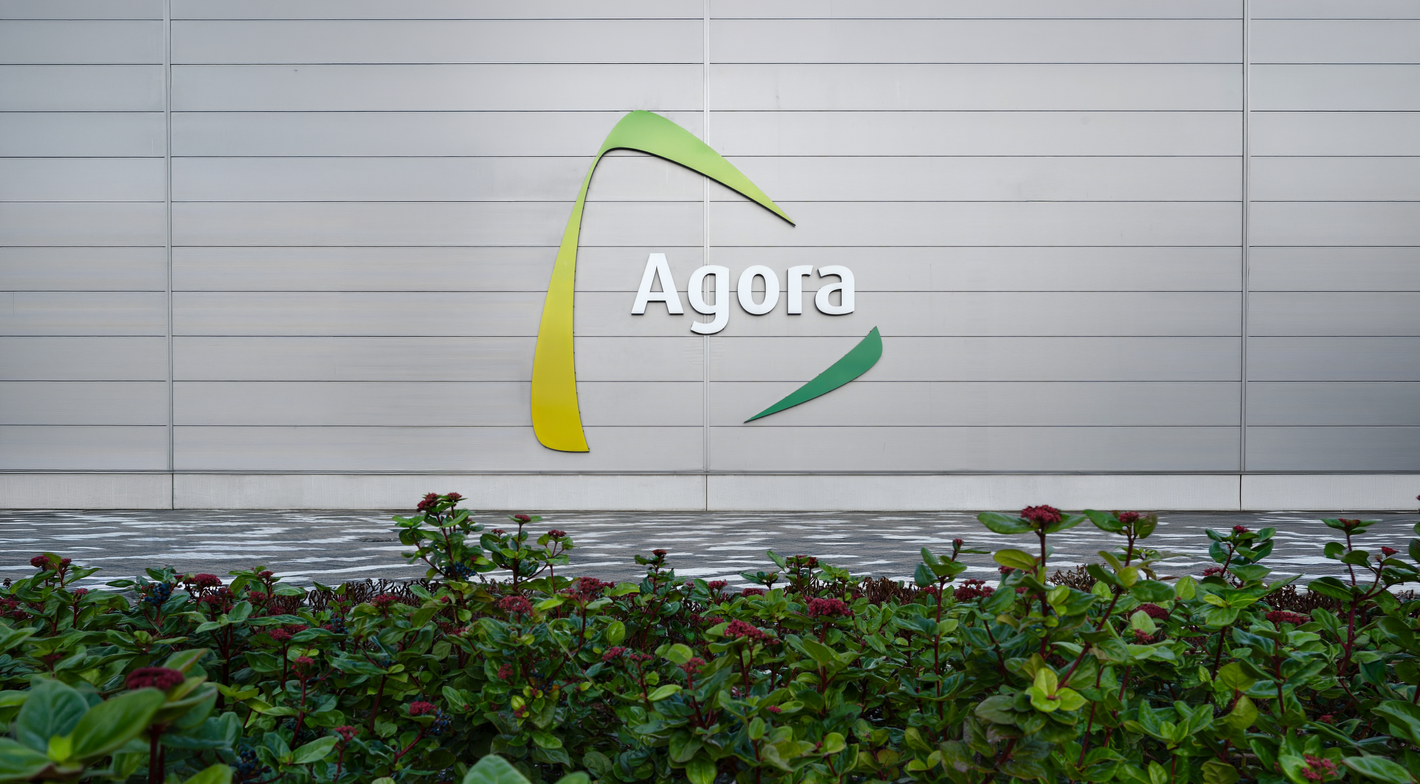 Logo "Agora" op witte gevel met groen gele accent; struiken op voorgrond