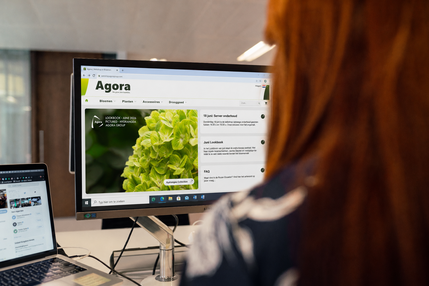 Persoon bekijkt op desktopmonitor de Agora-webshop met natuurafbeelding in kantooromgeving