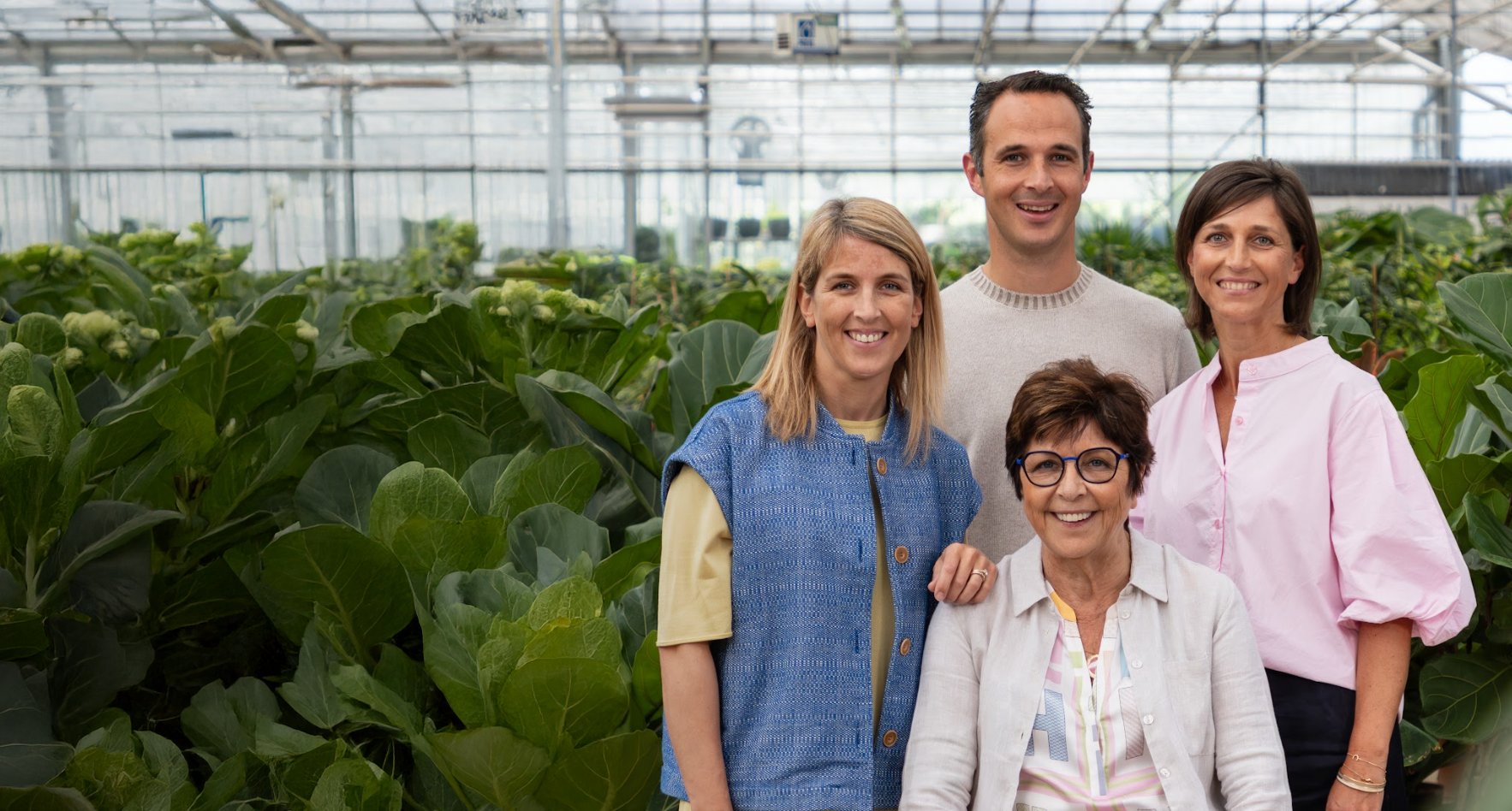 Vier mensen poseren in een kas tussen grote groene planten.