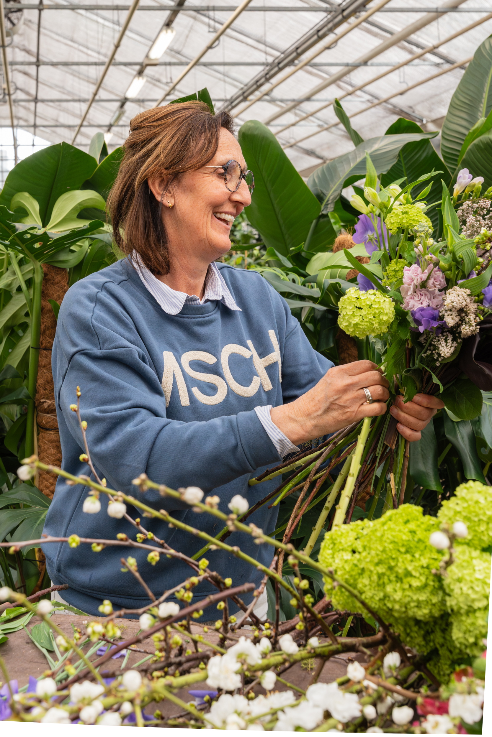 Vrouw in kas schikt groot boeket met paarse en groene bloemen