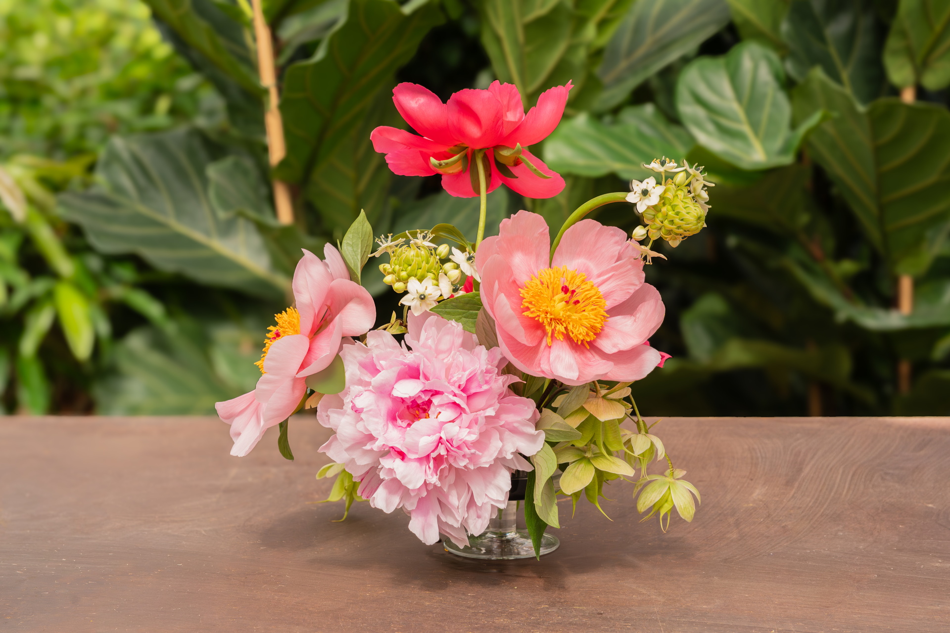 Klein boeket roze en rode bloemen in een vaasje op houten tafel, groene achtergrond