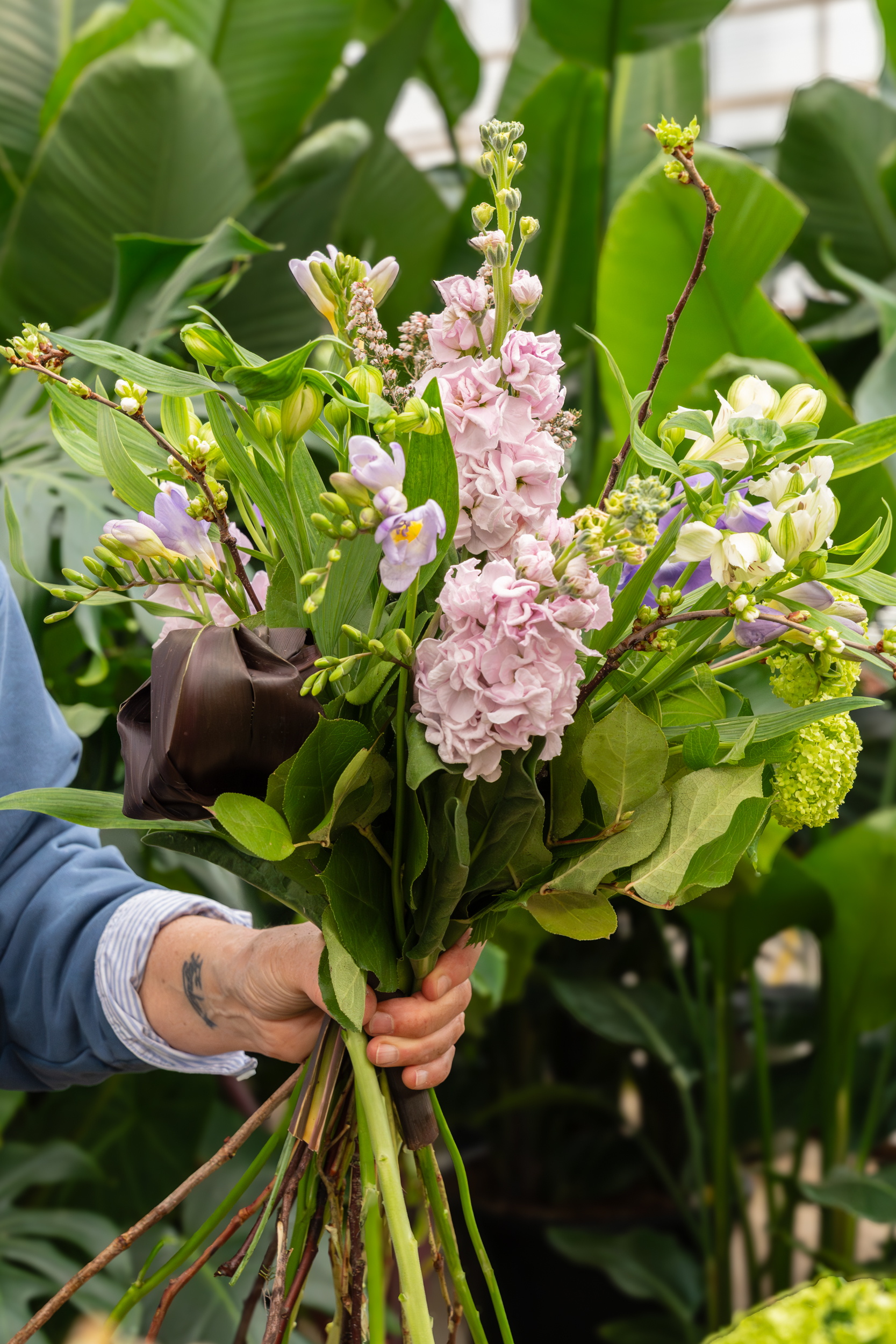 Handen houden een gemengd boeket met roze bloemen en groen blad in kas.