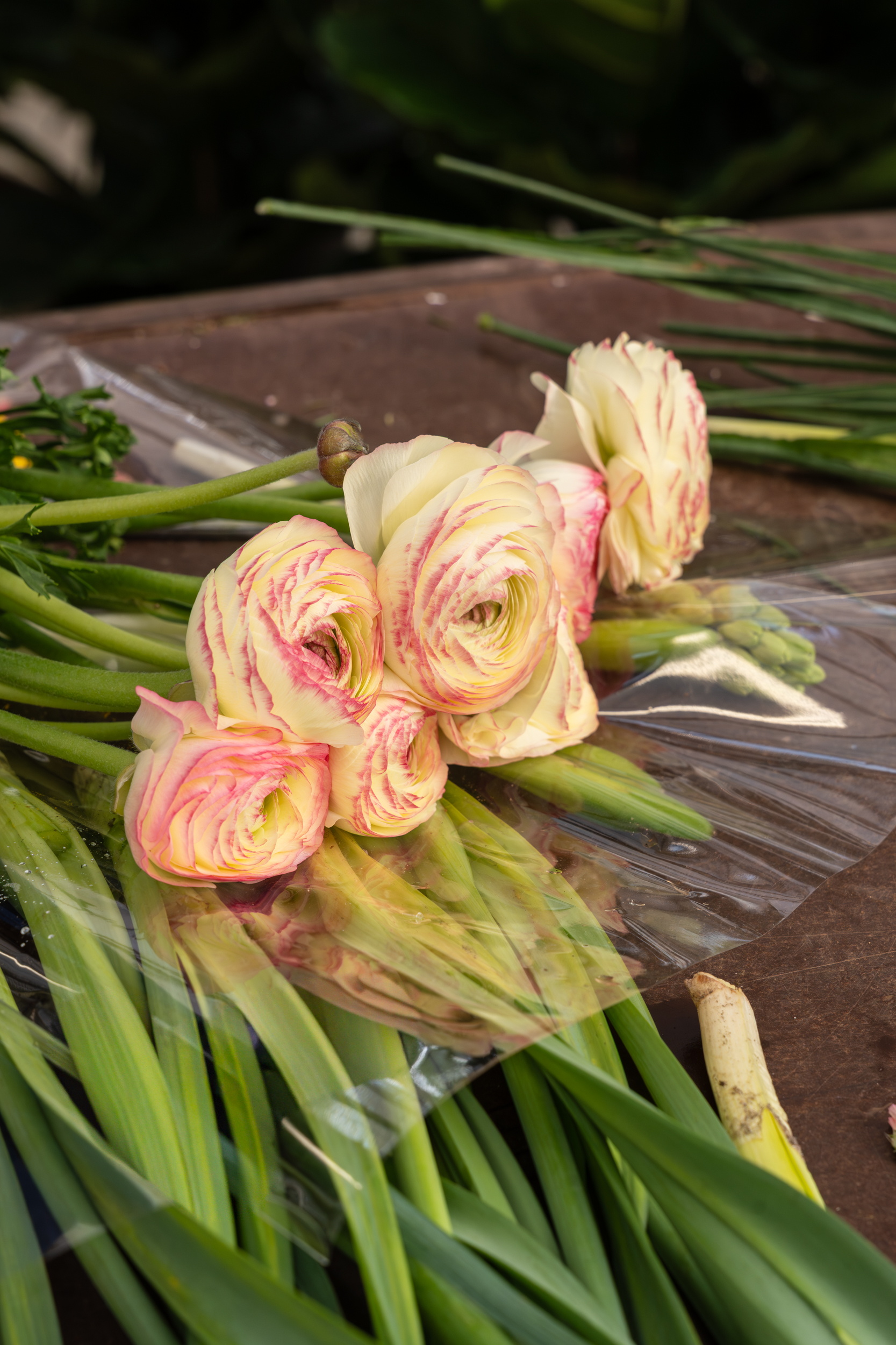 Roze en gele ranonkels met lange groene stelen op houten tafel