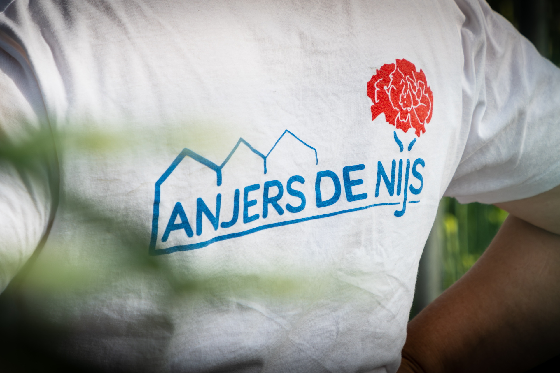 Wit T-shirt met logo en tekst “ANJERS DE NIJS” en rode anjer