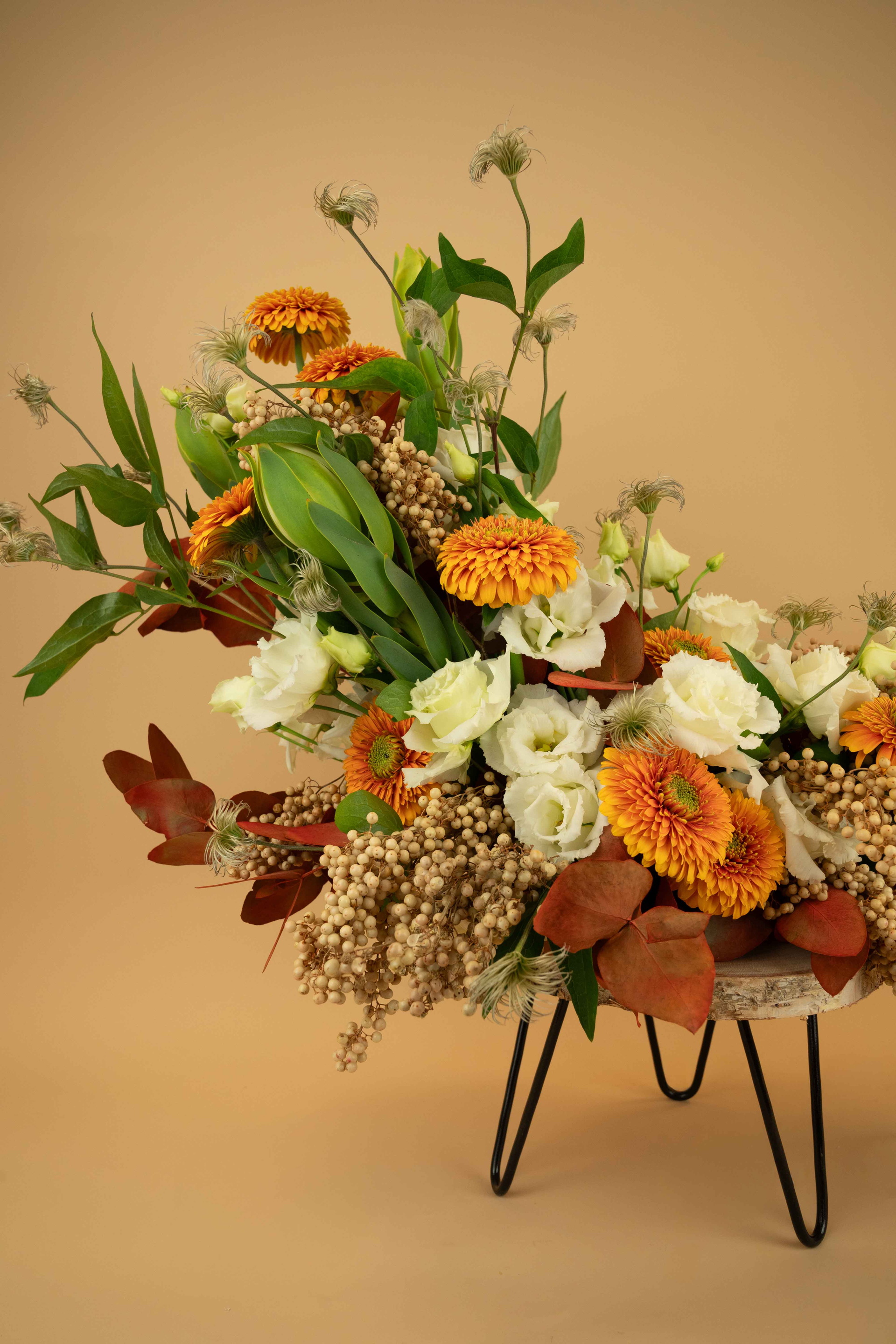 Bloemstuk met oranje en witte bloemen op zwarte standaard tegen beige achtergrond