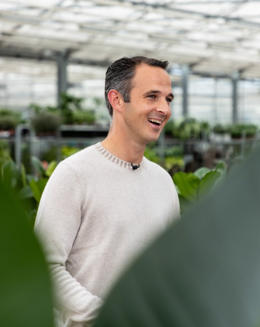 Lachende man in lichte trui in een kas met planten op de achtergrond