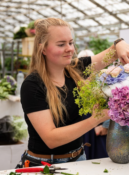 Bloemist maakt boeket in vaas met paarse hortensia en groen in kas.