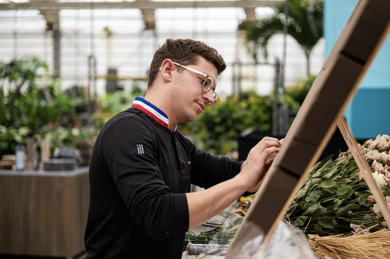Man met bril koopt groenten bij een marktstand in een kas.
