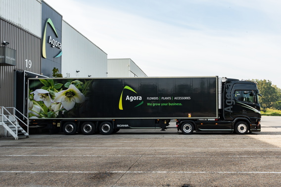Zwarte vrachtwagen met bloemenreclame bij magazijn, geparkeerd op terrein