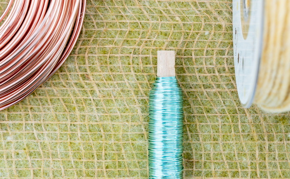 Koperen en gele draadspoelen op groen rasterpatroon, met turquoise spoel in het midden
