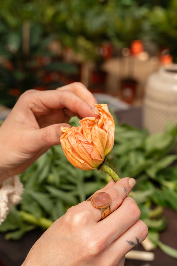 Handen plukken oranje bloemen bij een groentestalletje op een markt.