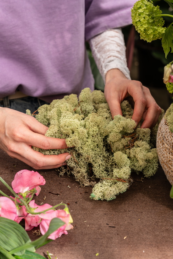 Handen schikken groene bloemkool op tafel naast roze bloemen en sla