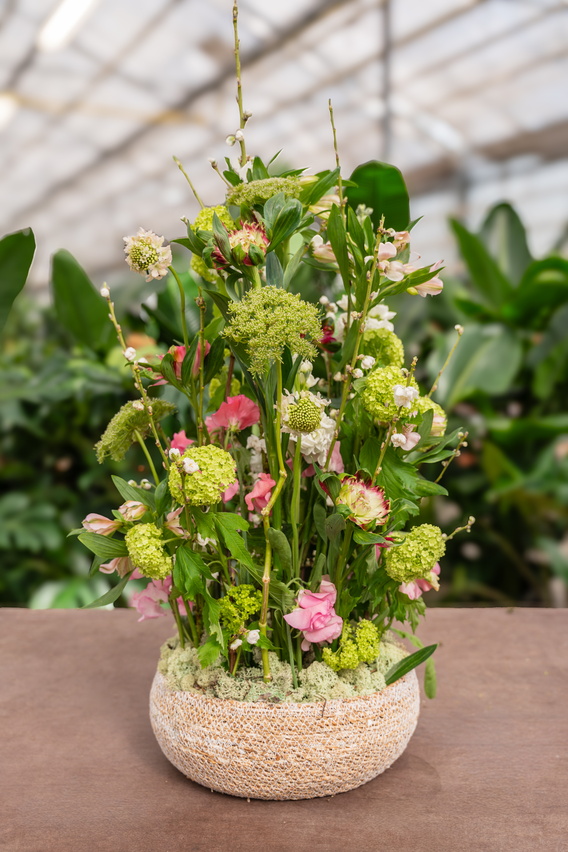 Groot bloemstuk met groene bladeren en roze bloemen in ronde vaas op tafel