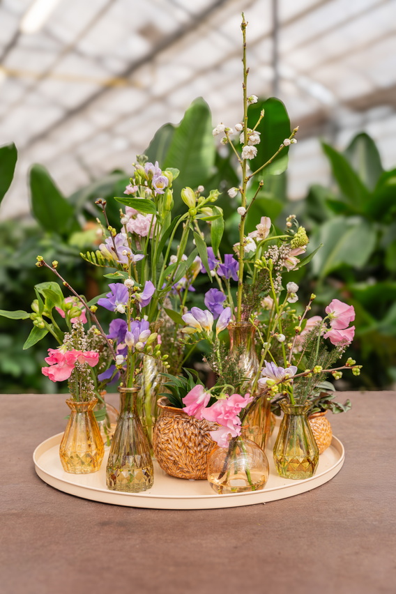 Gouden vaasjes met roze en paarse bloemen op houten tafel in kas