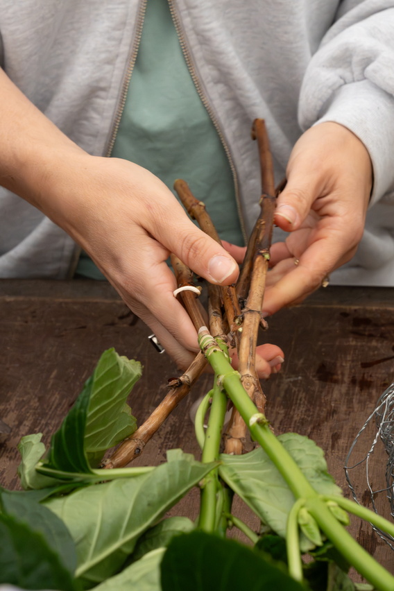 Handen binden groene bloemenstelen vast met touw op een houten tafel