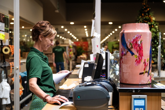 Kassière scant boodschappen bij kassa; grote roze kerstdecoratie op balie.
