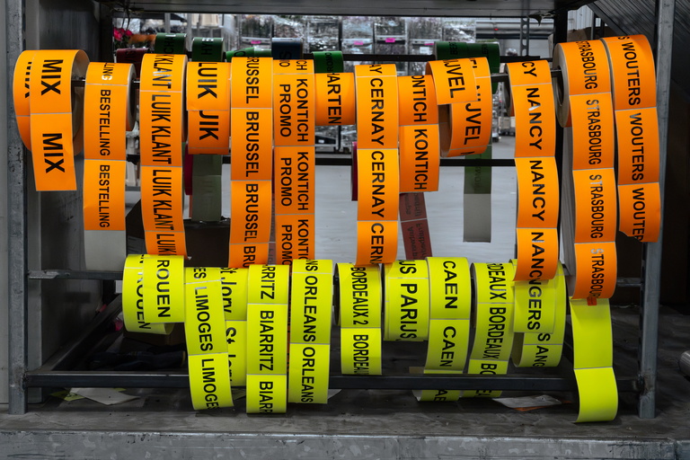 Rijen gelabelde cilinders in oranje en geel in een opbergvak, met zwarte tekst op tape.
