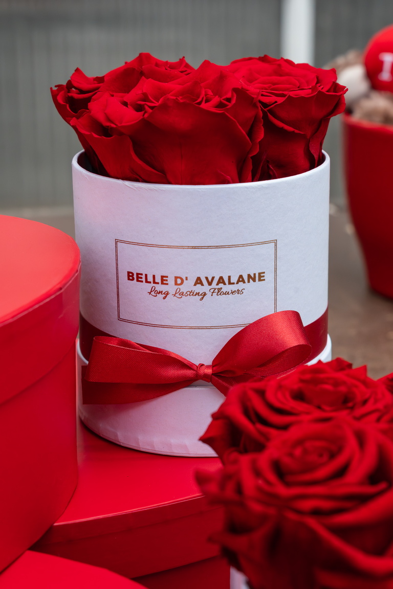 Witte ronde doos met rode rozen en rood lint, met rode cadeaudozen ernaast.