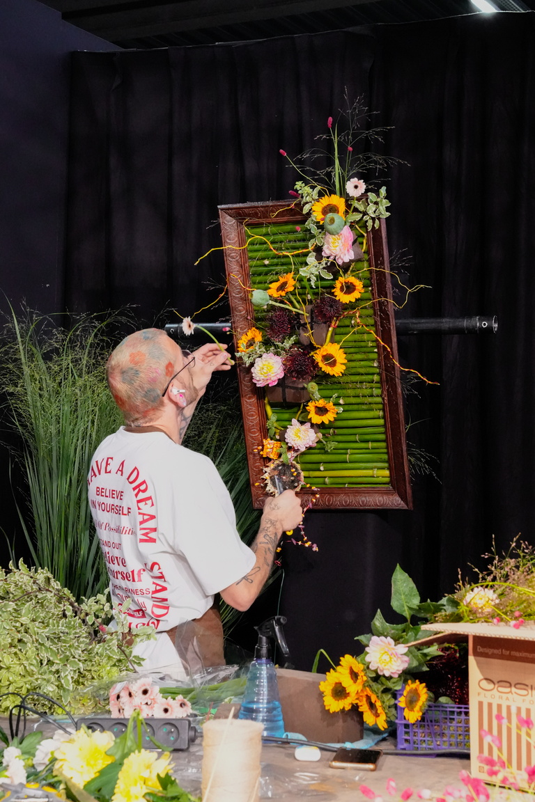 Florist creates a floral arrangement with sunflowers on a stage with a black background.