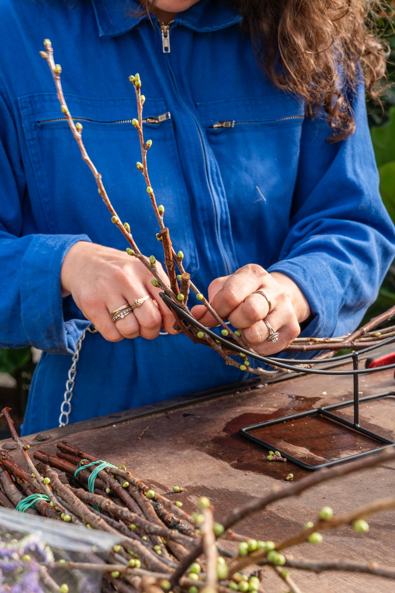 Vrouw in blauw shirt bindt twijgen vast op houten tafel buiten