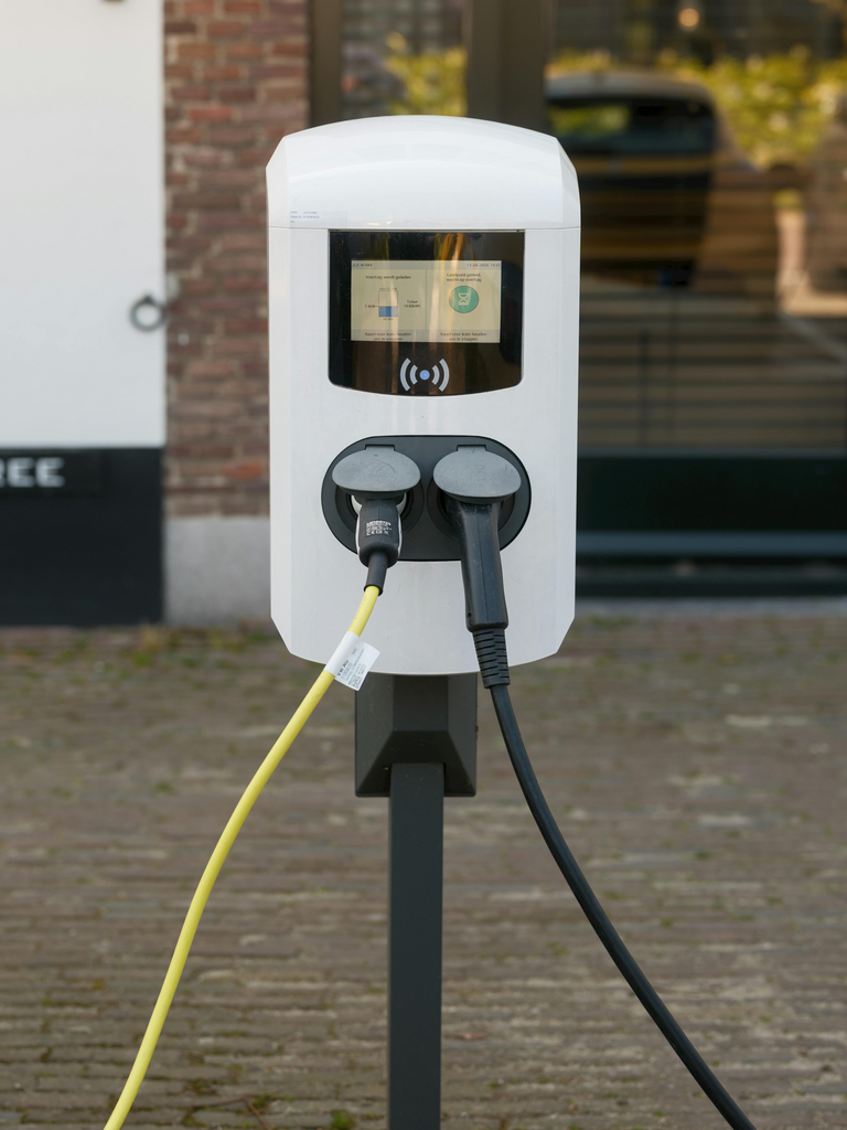 Witte laadpaal voor elektrische auto met twee kabels, geel en zwart, buiten op straat
