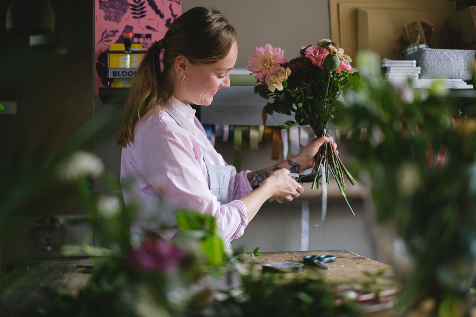 Bloemiste in atelier schikt boeket met tulpen en groen, zacht ochtendlicht.